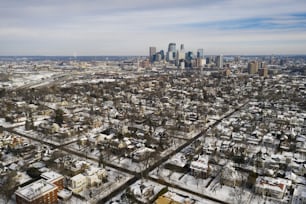 Aerial drone imagery of Minneapolis, Minnesota skyline viewed through a residential neighborhood on a partly cloudy day.