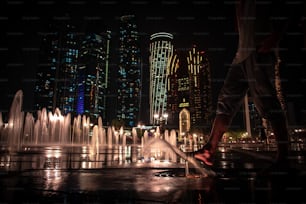 A low angle shot of a barefoot person walking on ground water fountains near Etihad Towers at night