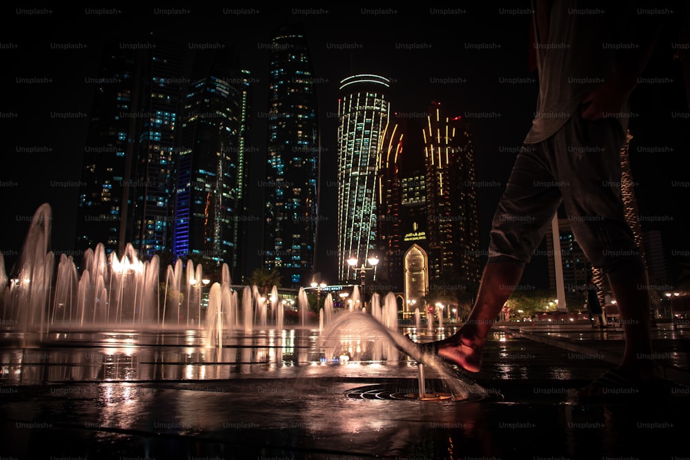 A low angle shot of a barefoot person walking on ground water fountains near Etihad Towers at night