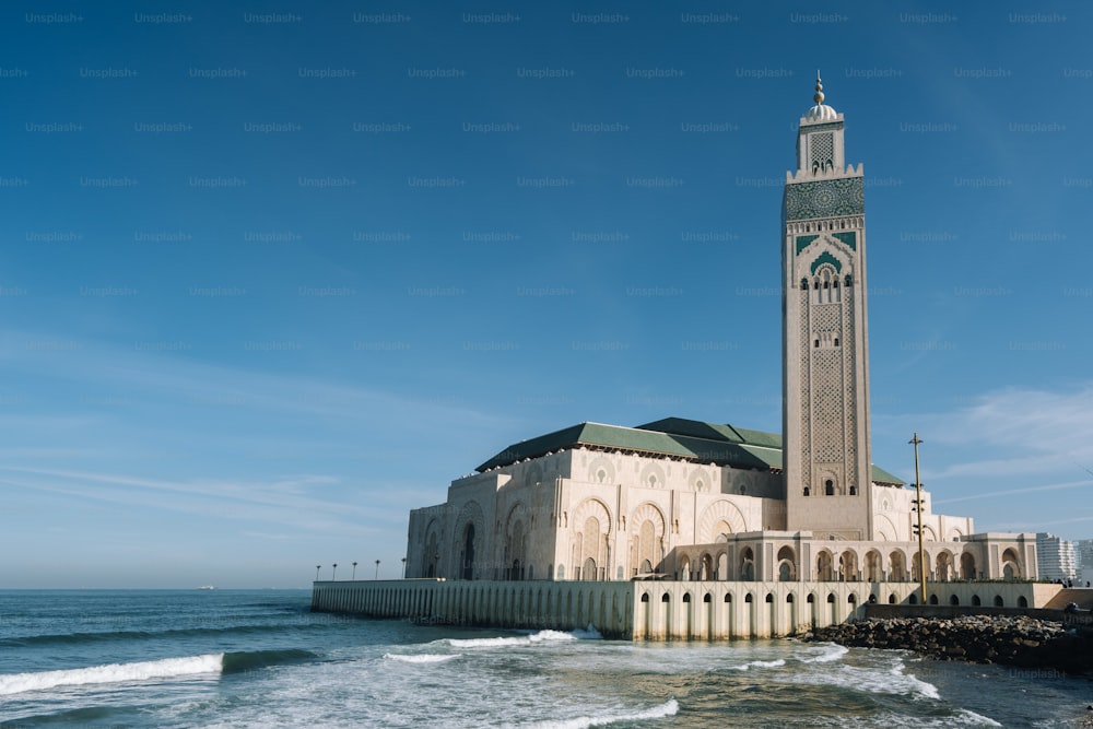 The Hassan II Mosque surrounded by water and buildings under a blue sky and sunlight