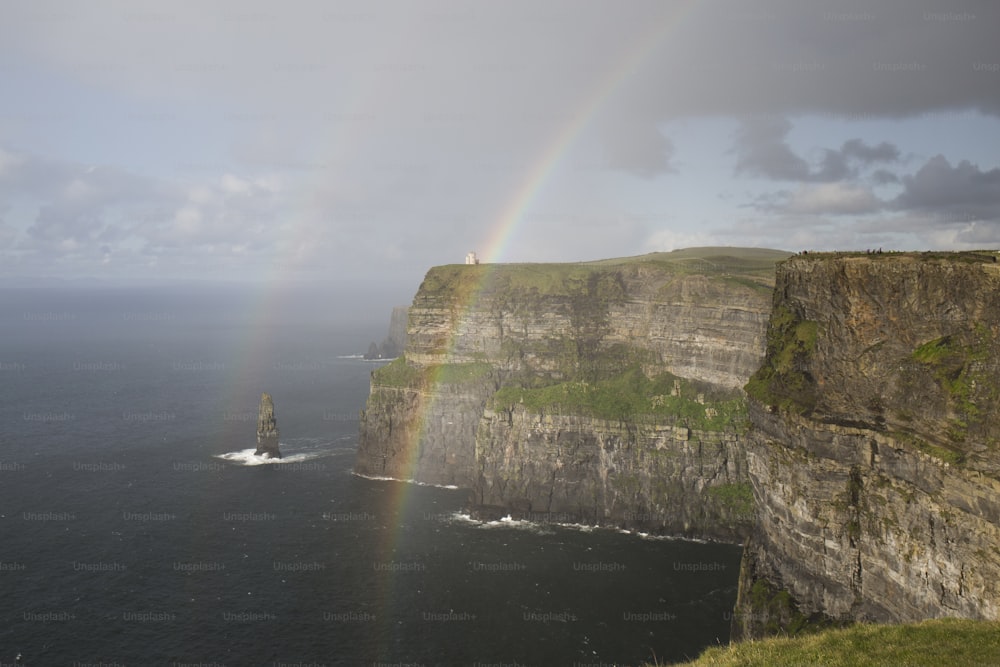 Paesaggio di incredibili scogliere di Moher in Irlanda con due arcobaleni, vegetazione verde e abbondante, mare blu, nuvoloso