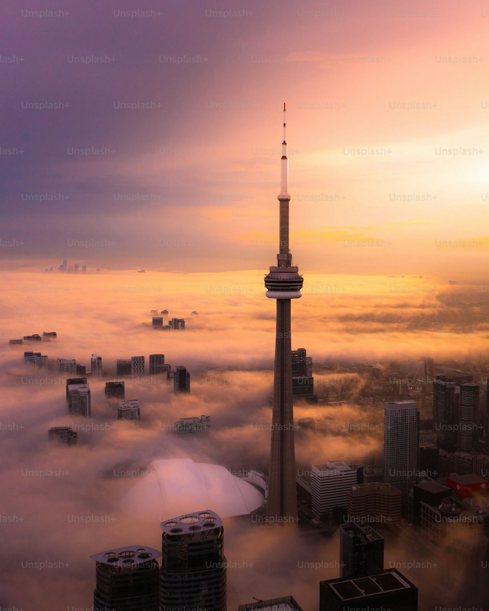 A vertical shot of the tower and other tall buildings during sunset covered with clouds, Toronto, Canada