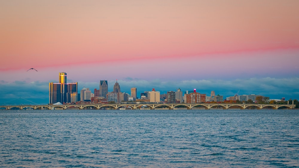A scenic cityscape of Detroit with a pink sunset sky and waterscape