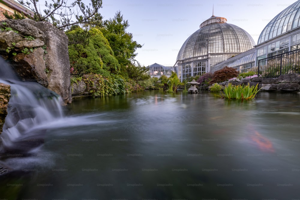 Der Wasserfall und der See in Langzeitbelichtung mit dem Anna Scripps Whitcomb Conservatory im Hintergrund.