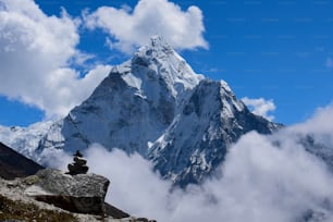 Une belle photo du mont Everest entouré de nuages et d’un empilement de rochers au premier plan