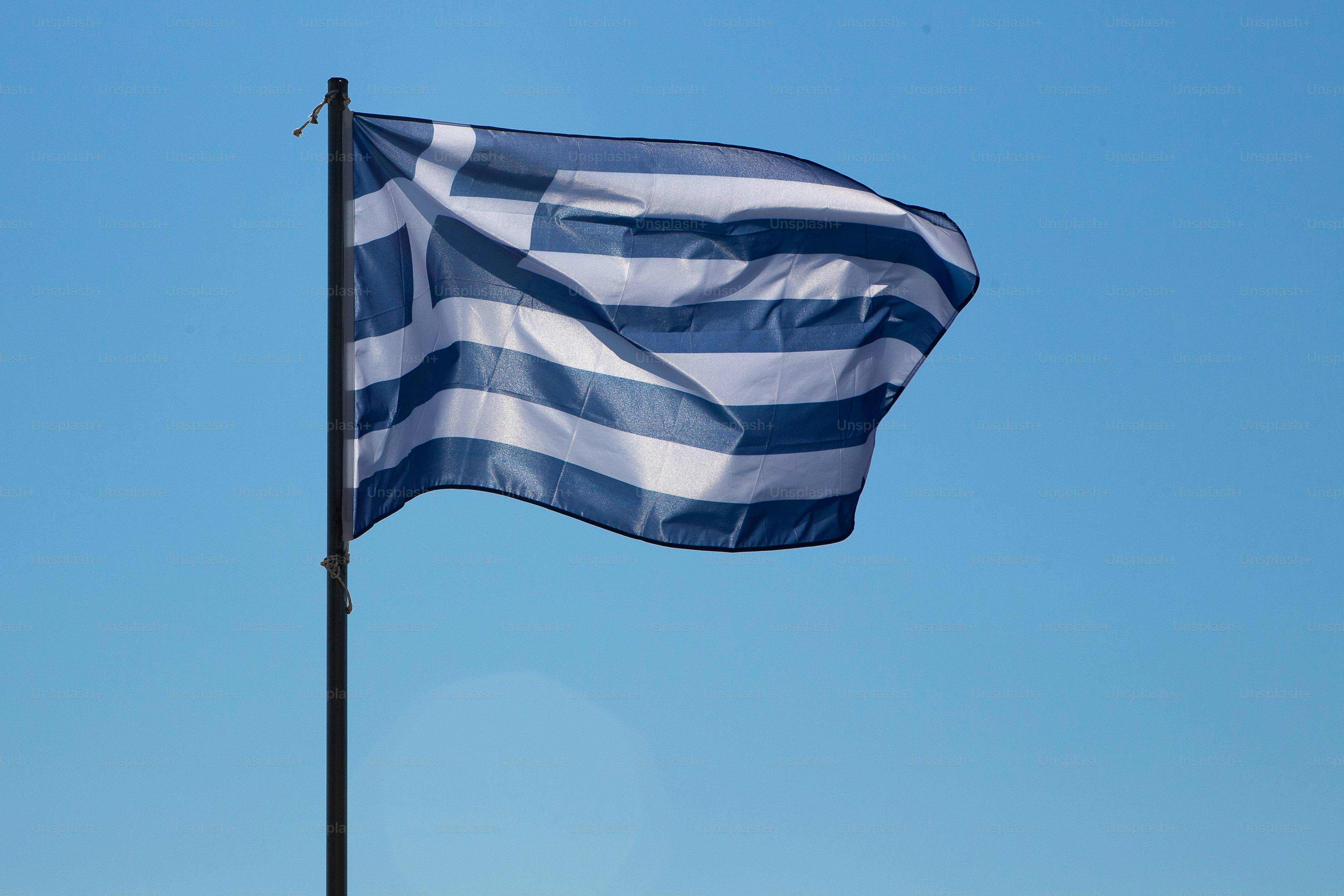 A low angled view on the national flag of Greece flapping in the wind on a flagpole. Isolated against a bright blue sky.