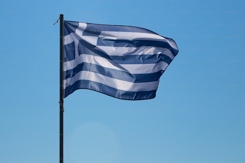 Una vista en ángulo bajo de la bandera nacional de Grecia ondeando al viento en un asta de bandera. Aislado contra un cielo azul brillante.