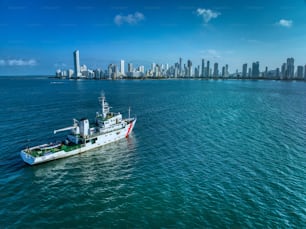 A white sailboat is sailing on the calm blue waters of a harbor in front of a picturesque city skyline