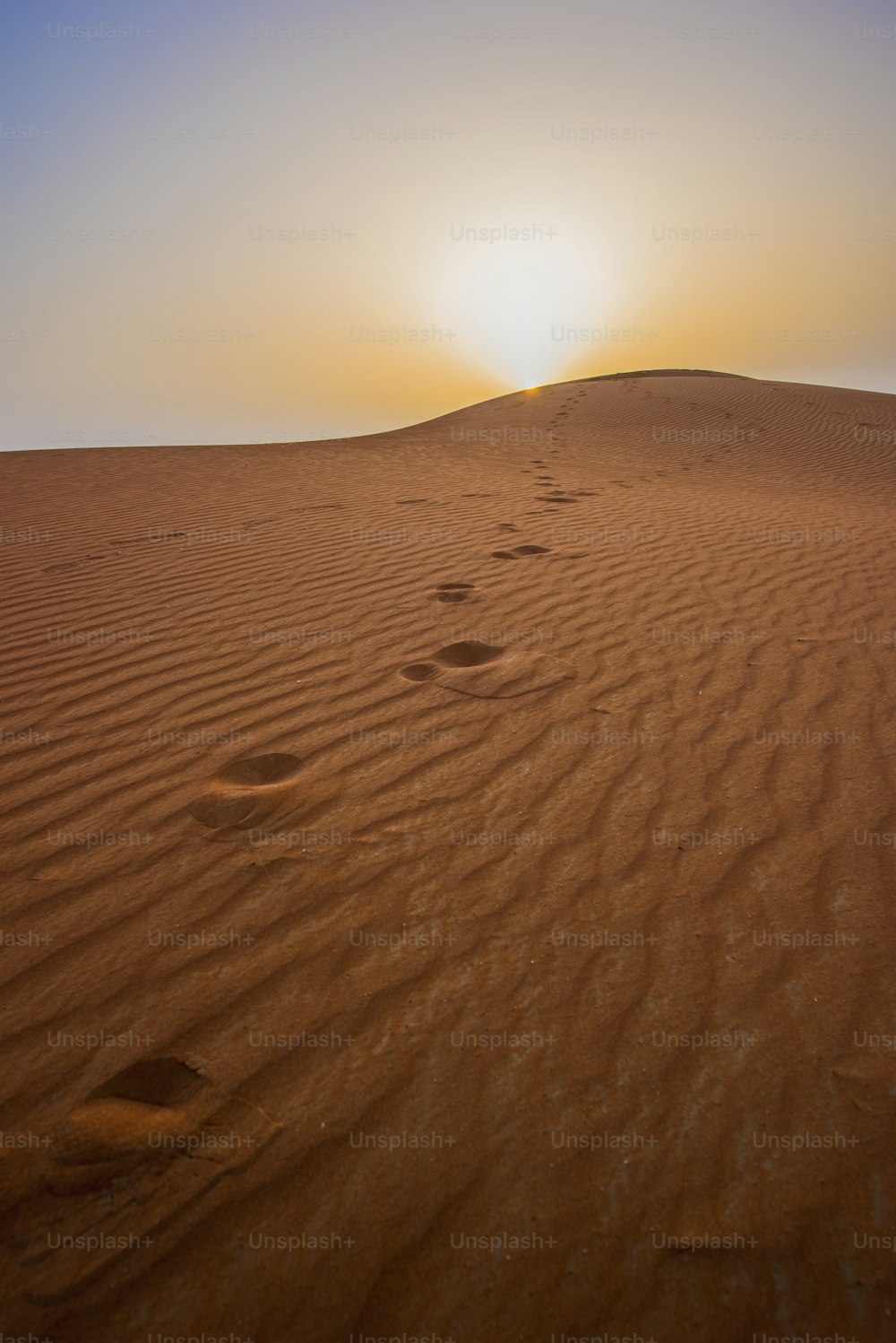 Beautiful desert sunrise with sun visible and sand dooms with sand pattern &walk triles