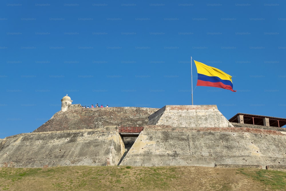 コロンビアのカルタヘナデインディアスにあるカスティージョサンフェリペデバラハスの要塞の風化した壁にコロンビアの旗が風に吹かれています。