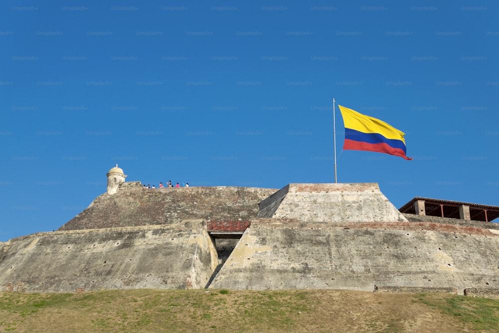 A Colombian flag is streaming in the wind over the weathered walls of the fortress of Castillo San Felipe de Barajas in Cartagena de Indias, Colombia.