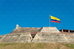 コロンビアのカルタヘナデインディアスにあるカスティージョサンフェリペデバラハスの要塞の風化した壁にコロンビアの旗が風に吹かれています。