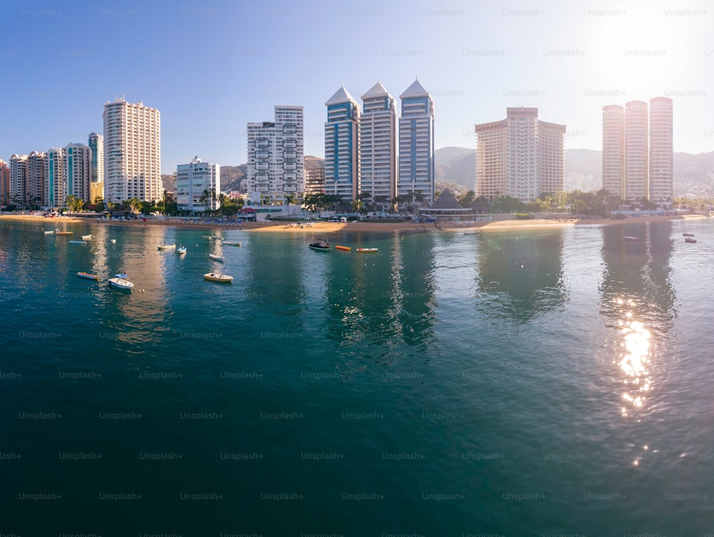 A sunny day in Acapulco, Mexico with boats sailing on the sea and tall buildings reflected in the water