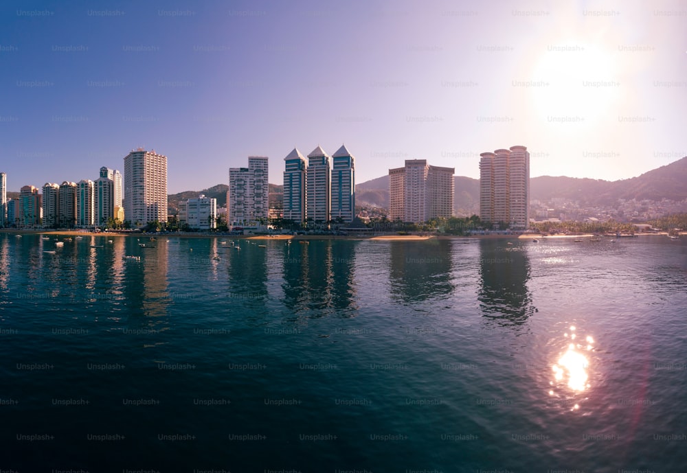 A bright scorching sun reflected in the water in the Acapulco Bay in Mexico with  buildings standing tall under a clear sky in the background