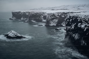 A picturesque winter landscape in Reykjavik, Iceland featuring a snow-covered lake and a rocky outcropping on the shore
