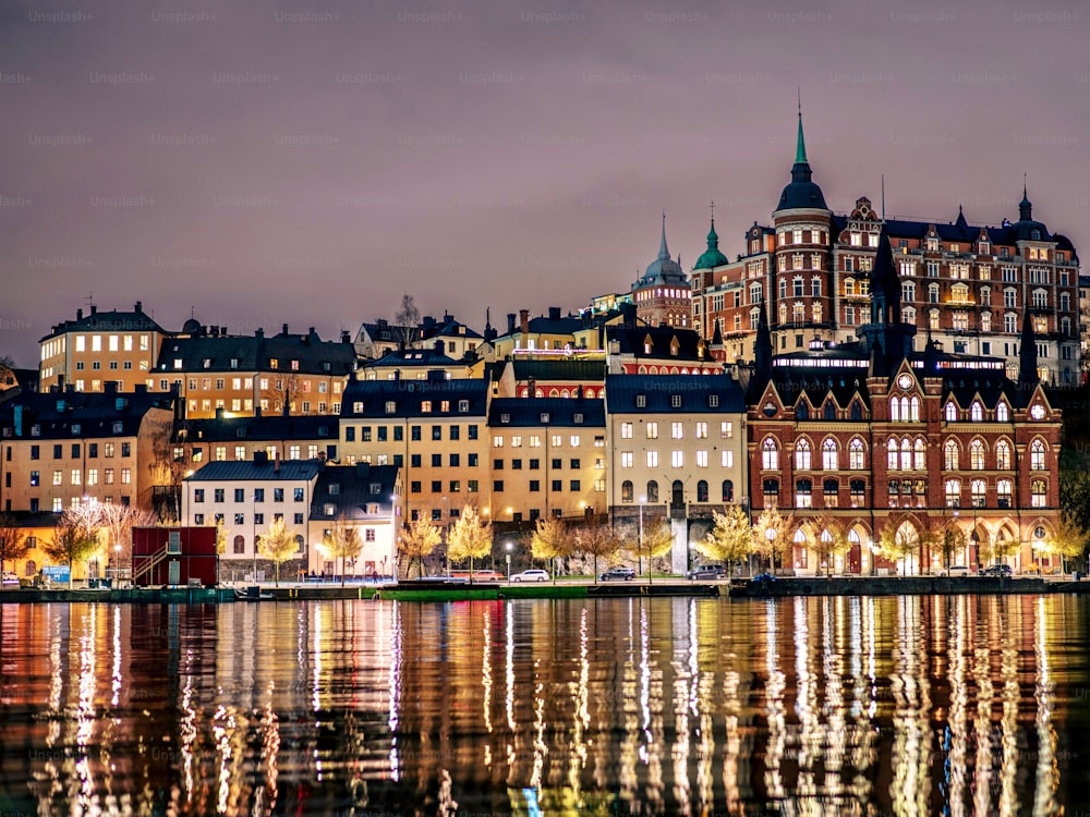 Illuminated buildings line the shore of a tranquil body of water in the evening in Stockholm, Sweden