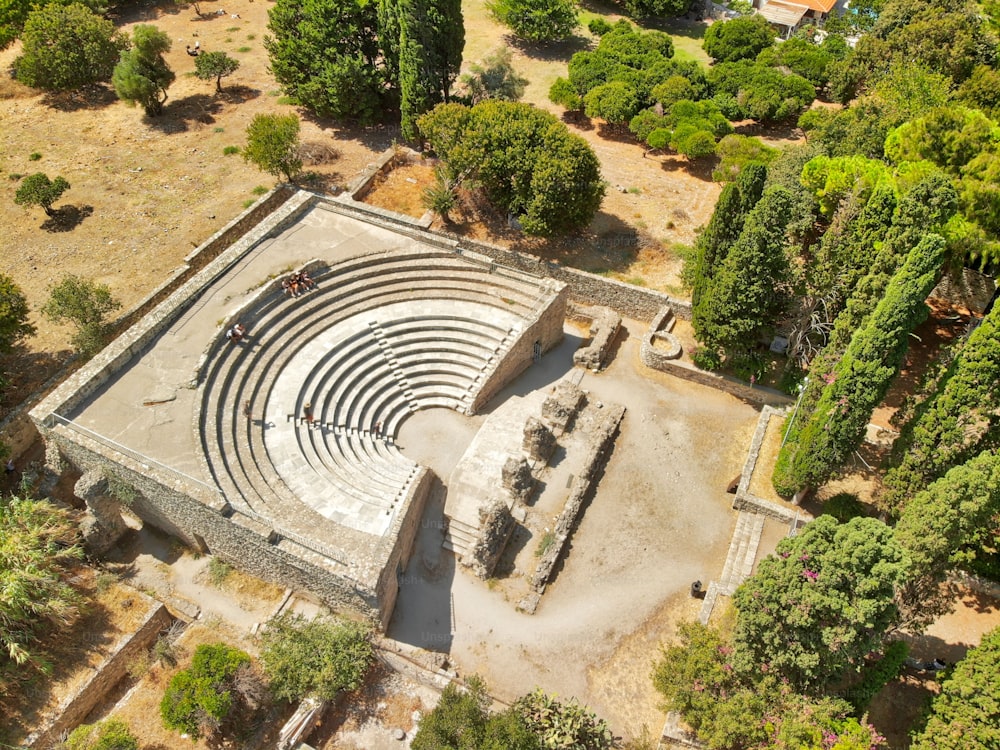 An aerial view of the historic Odeon theater in Kos, Greece surrounded by a lush forest of trees