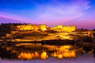 Indisches Wahrzeichen - Amer Fort (Amber Fort) nachts beleuchtet - eine der Hauptattraktionen in Jaipur, Rajastan, Indien, die sich in der Dämmerung im Maota-See spiegelt
