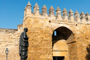 Detalhe de um dos portões arábicos (Puerta de Almodóvar) na muralha medieval que rodeia a cidade velha de Córdoba em um claro dia de primavera, com a estátua do filósofo Sêneca em pé à sua frente.