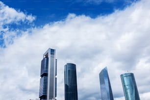 Modern skyscrapers in the CTBA (Cuatro Torres Business Area) in Madrid against a cloudy blue sky.