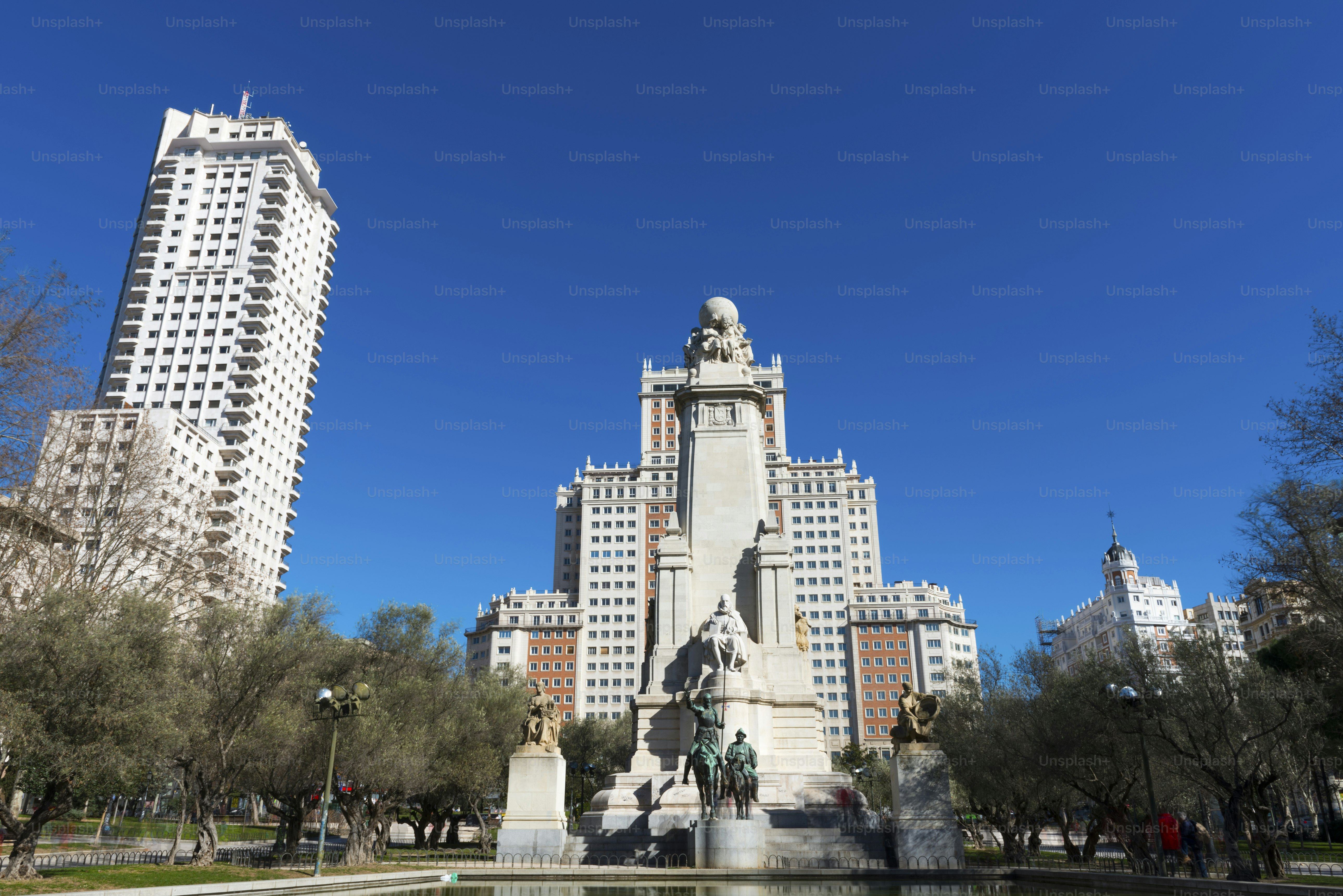 Wide angle view of Plaza de España and the surrounding historic buildings on a sunny winter morning, with the statue commemorating Cervantes in the foreground.