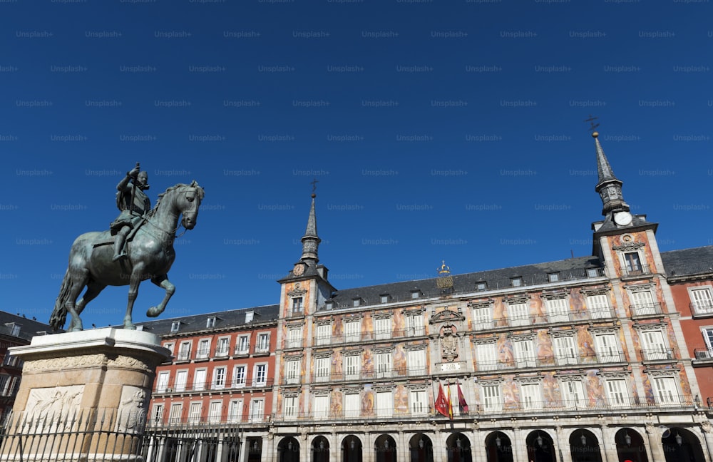Weitwinkelansicht der Plaza Mayor (Hauptplatz) von Madrid, mit den Fresken auf der Casa de la Panaderia und der Statue von Felipe III. aus dem 17. Jahrhundert, die den Platz überragt.