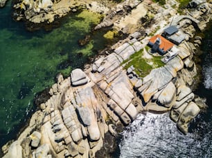 Rocas, barcos y pequeño faro en una pequeña isla de Galicia, España.