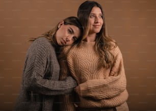 two women hugging each other in front of a brown background