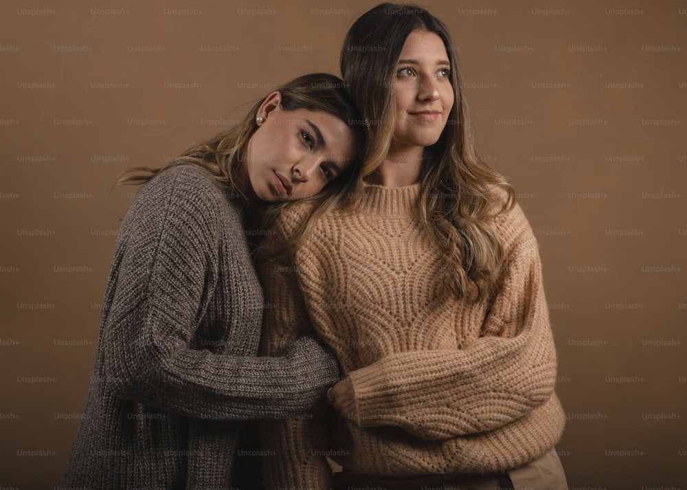 two women hugging each other in front of a brown background