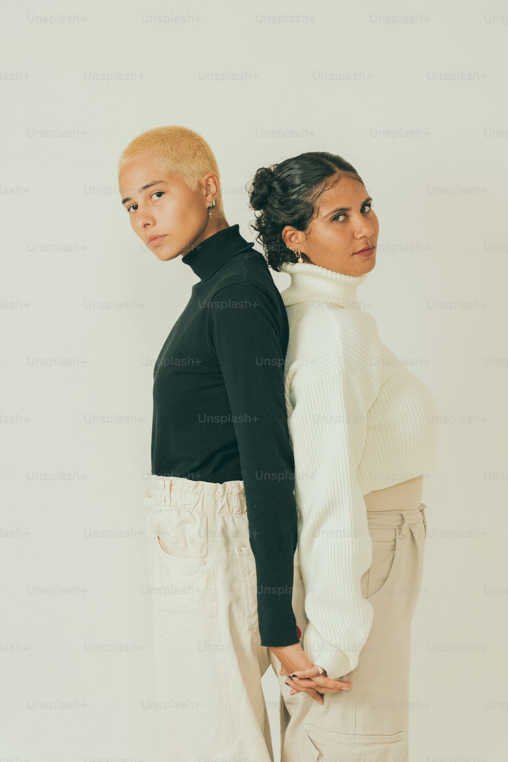 two women standing next to each other in front of a white wall