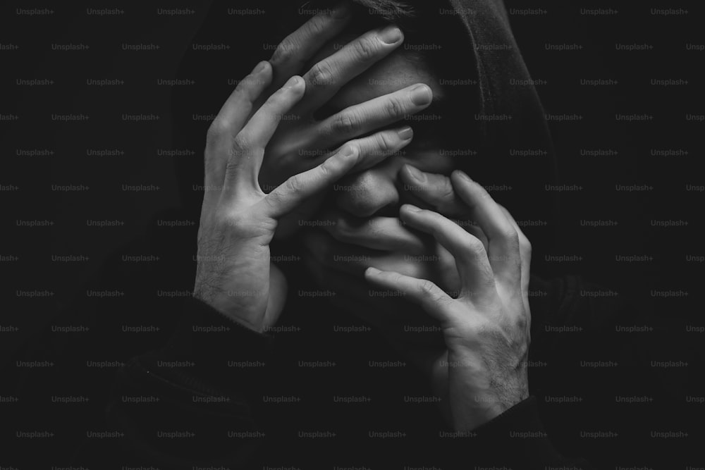 a black and white photo of a person covering their face with their hands