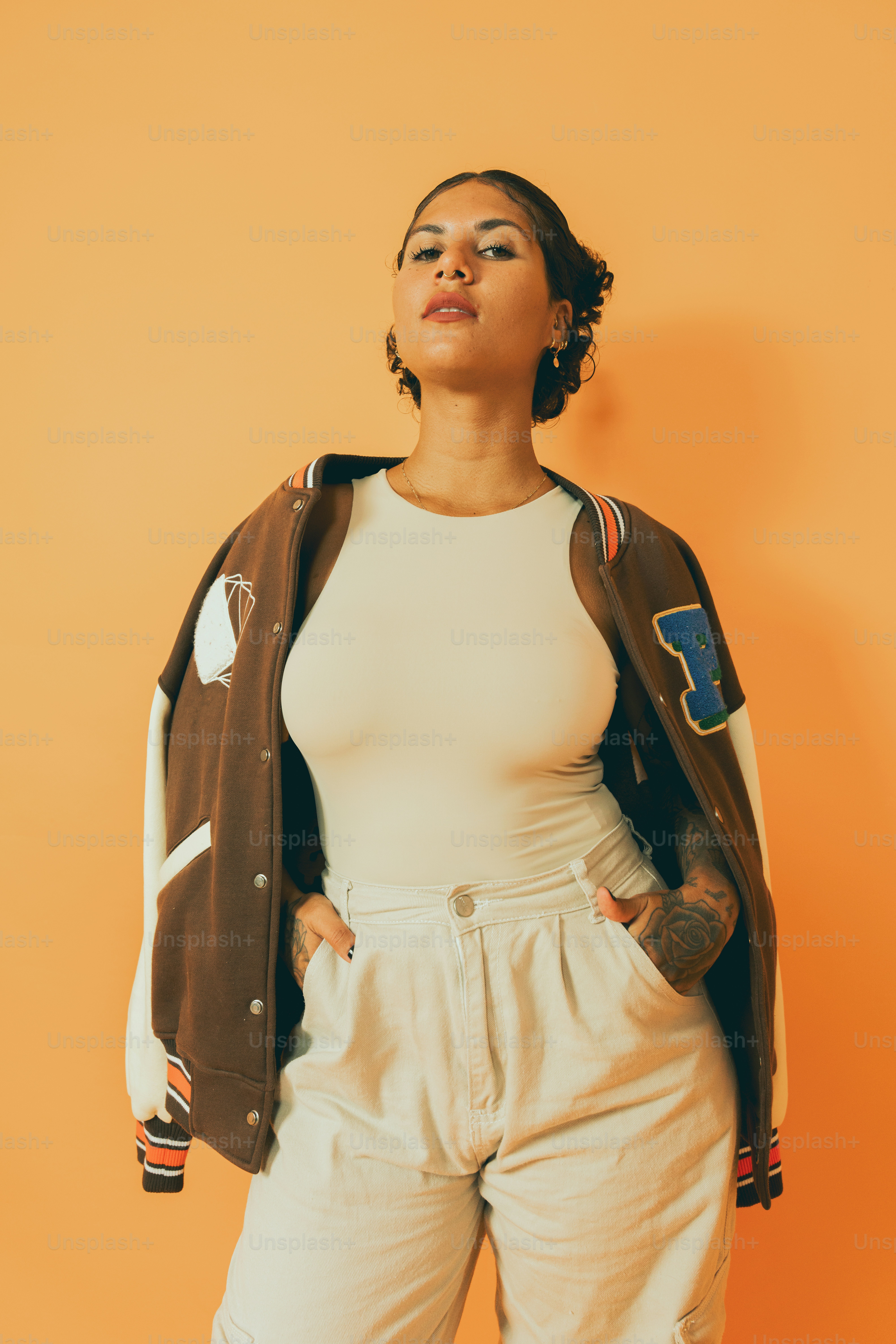 A woman standing in front of an orange wall photo – Hands in pocket ...