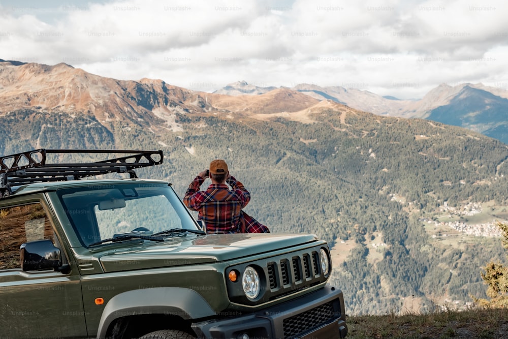 a man standing on top of a mountain next to a green jeep
