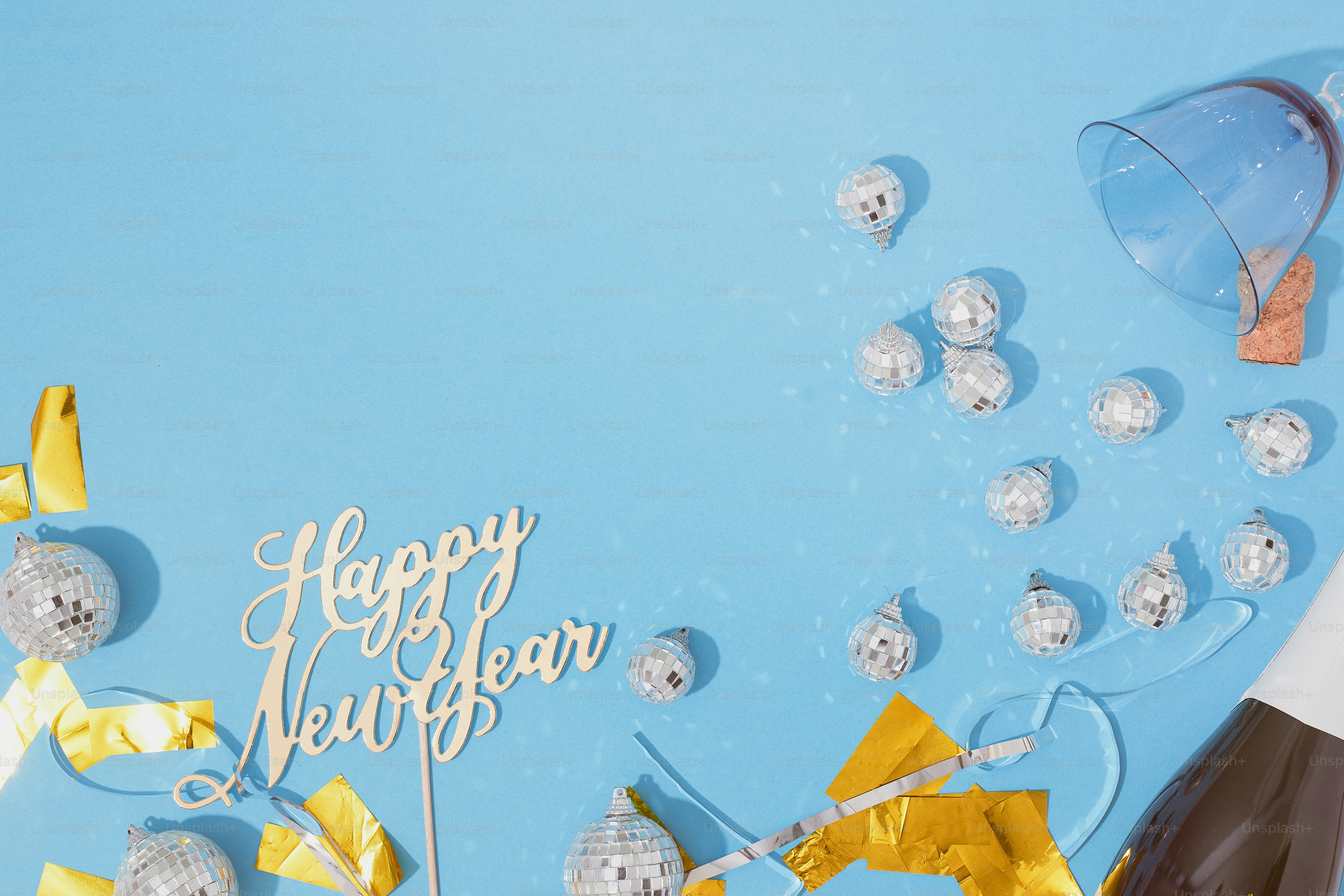 Overhead of blue surface and disco balls with happy new year text and champagne bottle and negative space