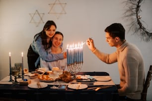 한 남자가 두 여자와 함께 탁자 위에 메노라에 불을 붙이고 있다