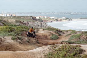 a man riding a motorcycle down a dirt road next to the ocean