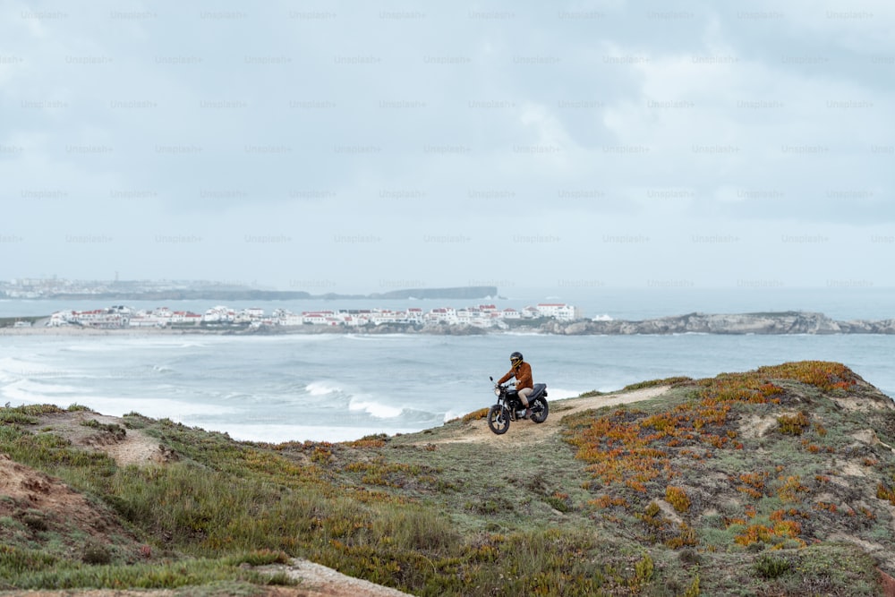un uomo in sella a una motocicletta giù per una collina vicino all'oceano