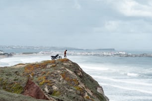 a man standing on top of a hill next to a motorcycle