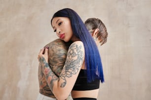 a woman with blue hair hugging a man with tattoos