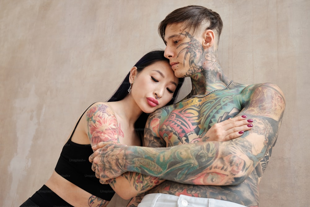a tattooed man and woman embracing each other