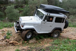 a white jeep with a black roof is parked in the woods