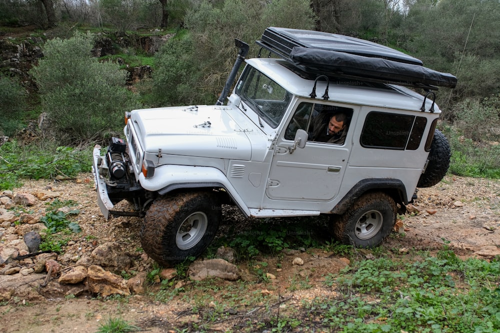 Une jeep blanche avec un toit noir est garée dans les bois