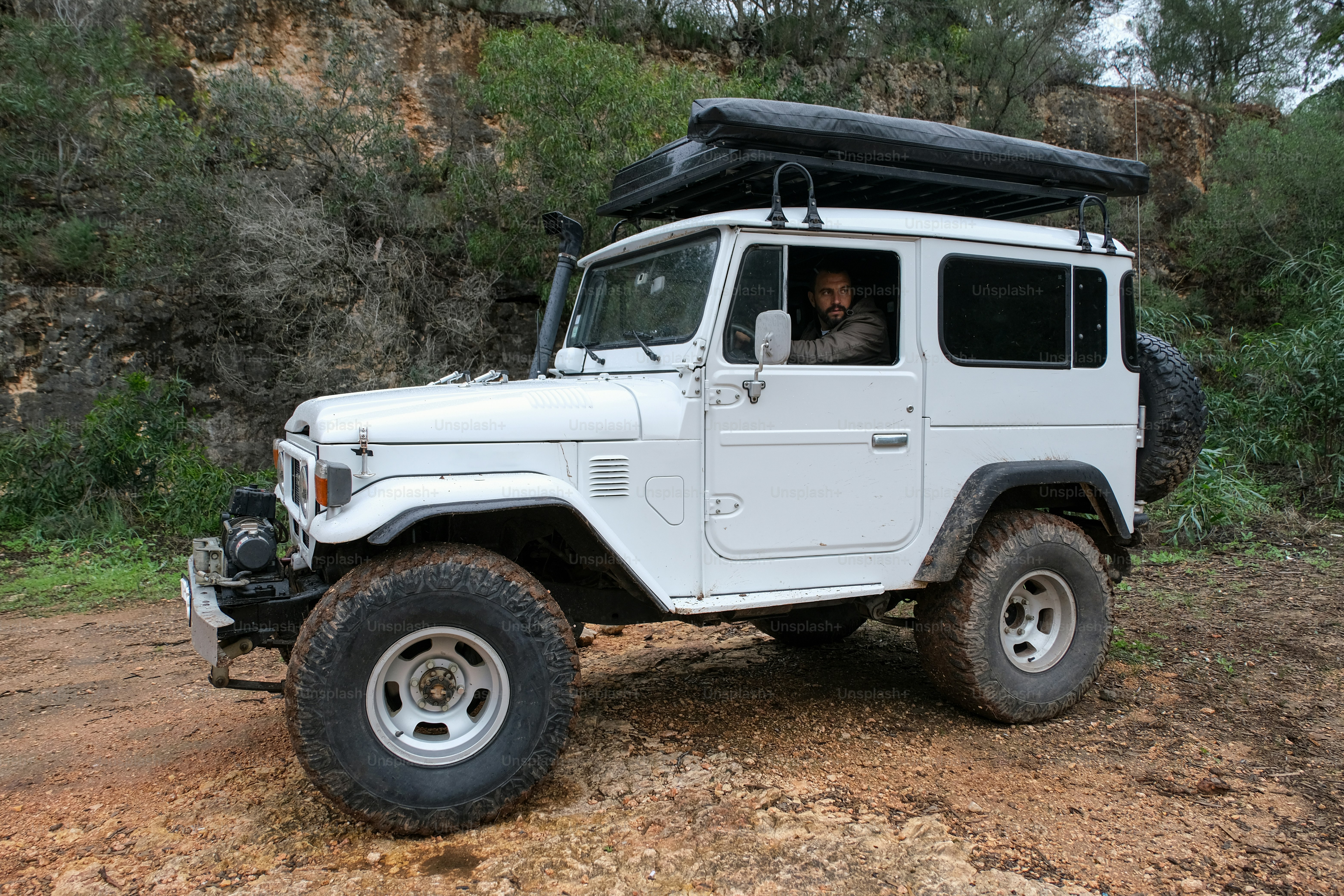 a white jeep with a black roof and a man in the driver's seat