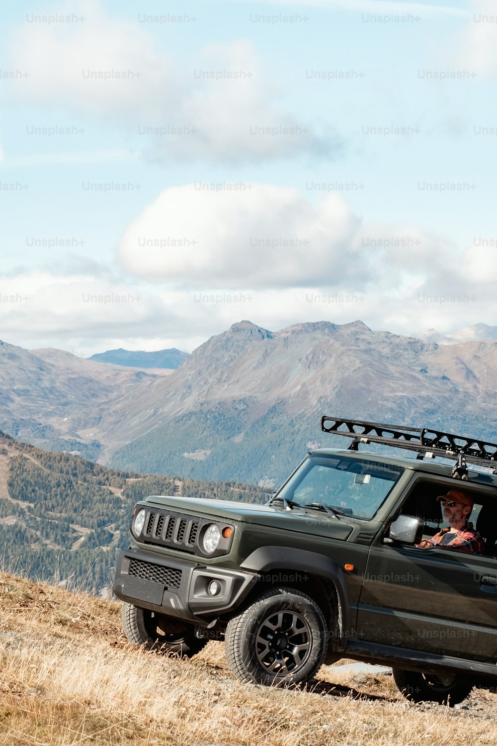 a green jeep driving down a hill with mountains in the background