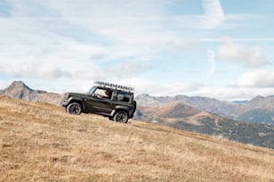 Ein Jeep, der einen Hügel mit Bergen im Hintergrund hinauffährt