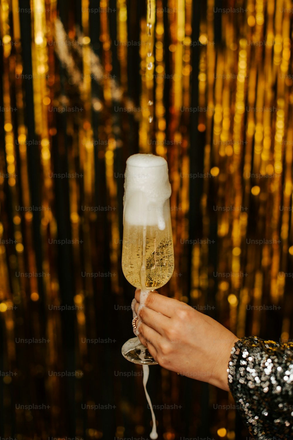 a person holding a glass of champagne in front of a gold background