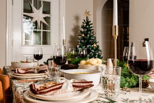 a table set for a holiday dinner with a christmas tree in the background