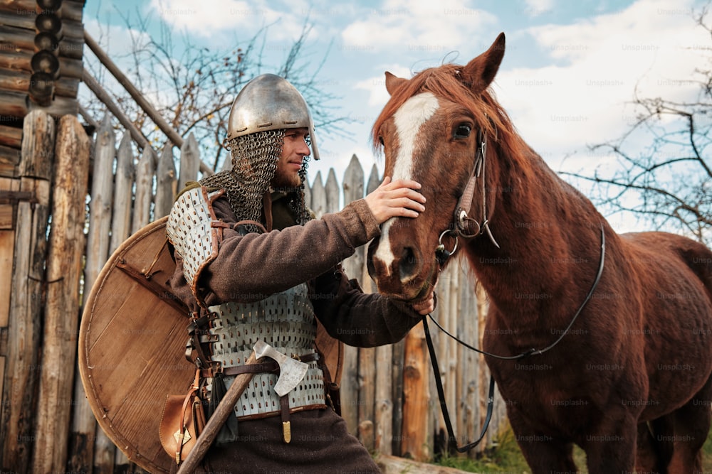 Un hombre con un traje medieval acariciando a un caballo