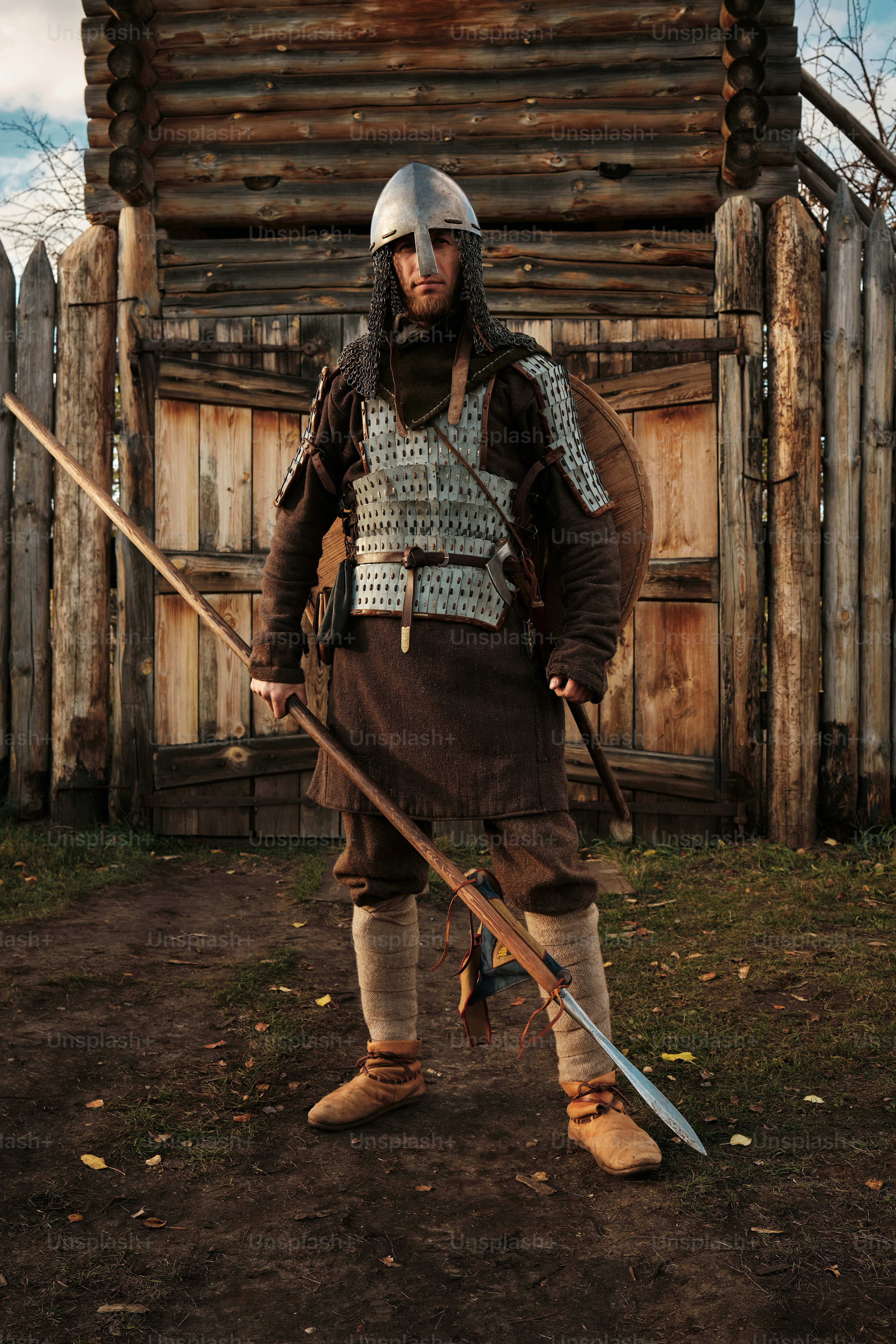 Portrait of a medieval guard with a spear near a wooden gate of a medieval settlement