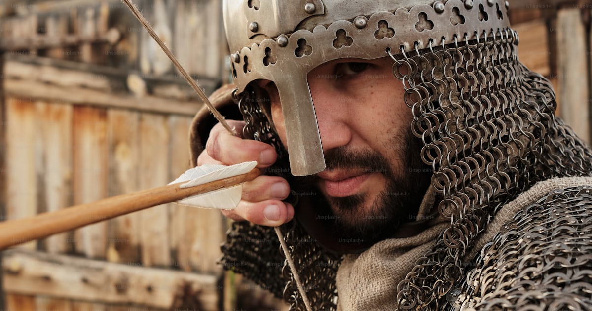 A man in a chain mail outfit holding a wooden stick photo – Archer ...